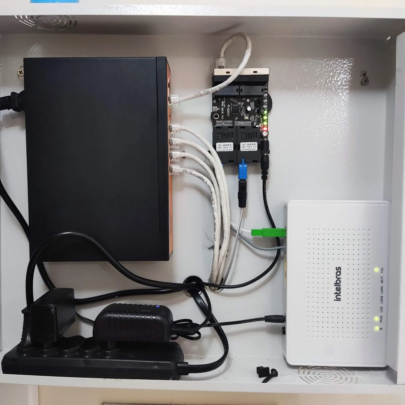 Quadro de rede instalado pela L&L com switch, conversores de fibra óptica e ONT Intelbras, cabos organizados